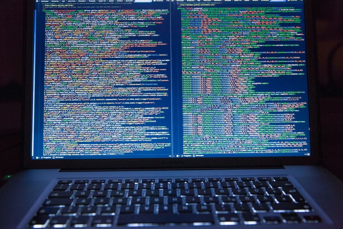 Laptop screen showing lines of colorful source code in a dark room