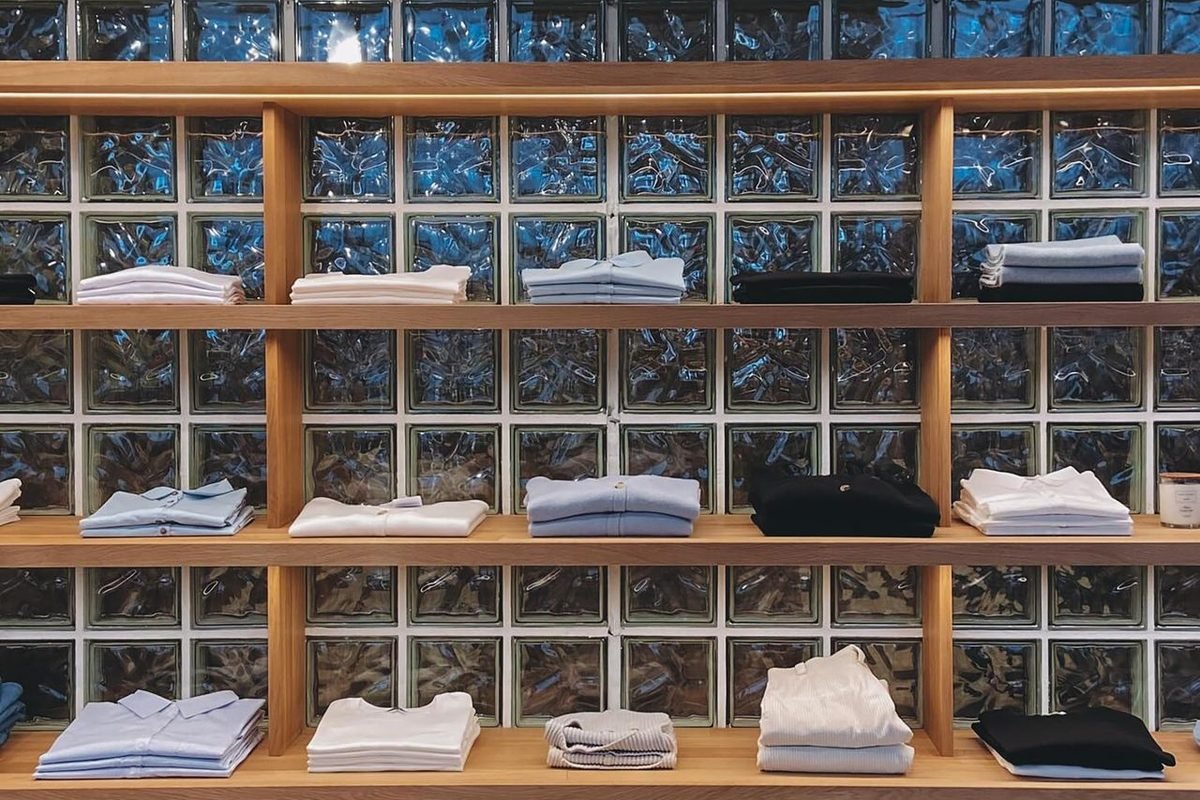 Folded shirts on wooden shelves in front of a glass block wall