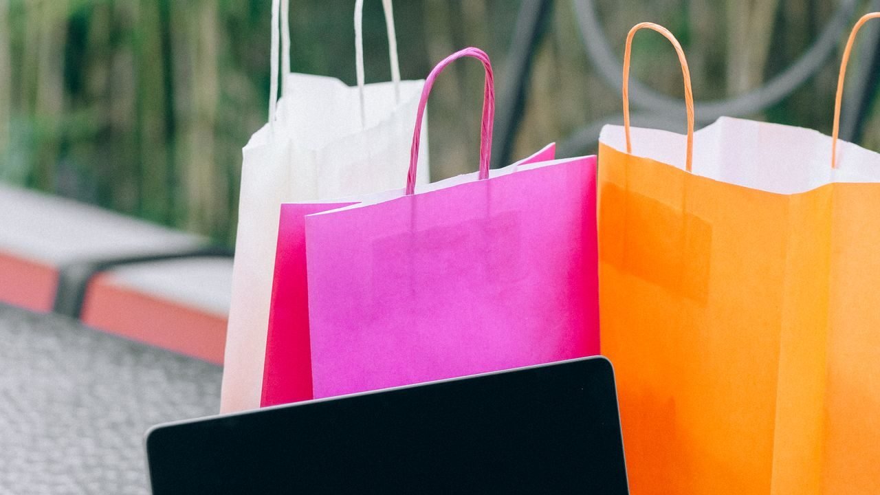 Laptop showing an online store next to colorful paper shopping bags
