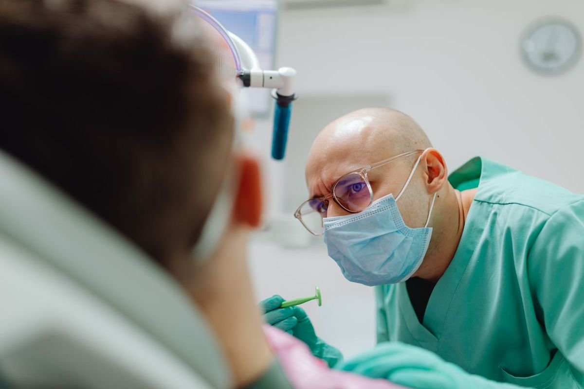 Dentist in a surgical mask and green scrubs treating a patient