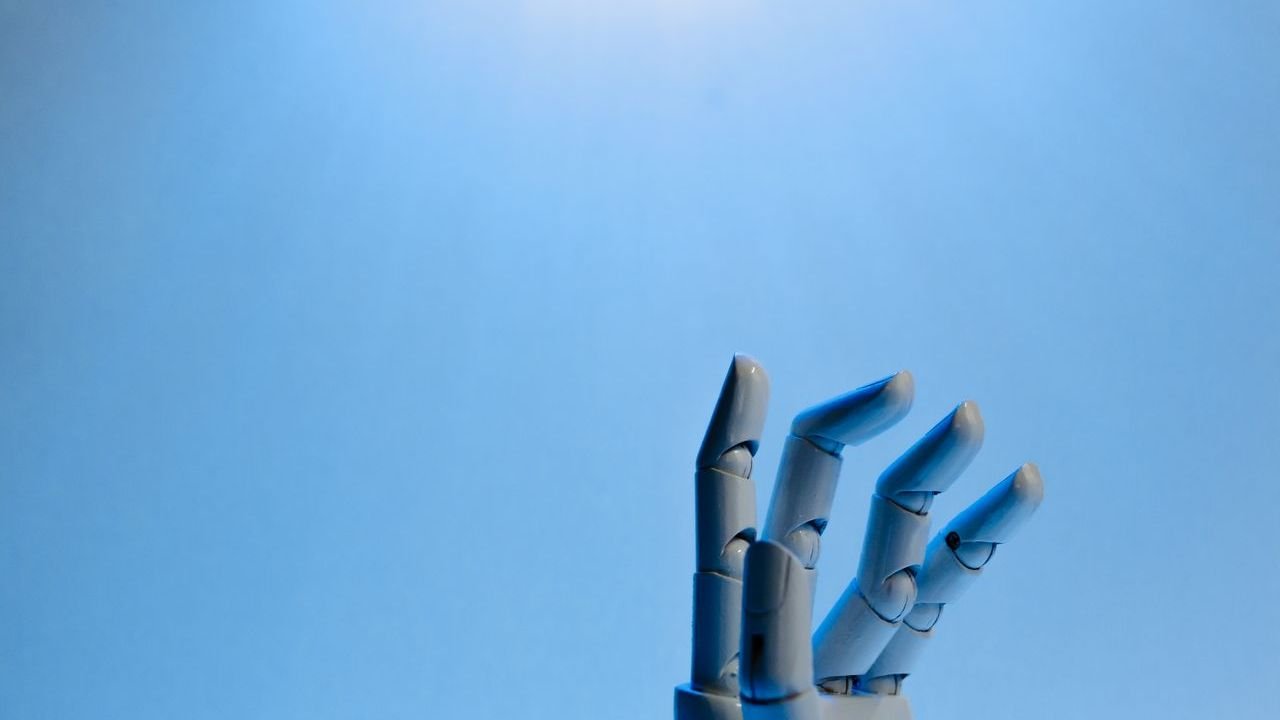 Blue robotic hand reaching up against a clear sky