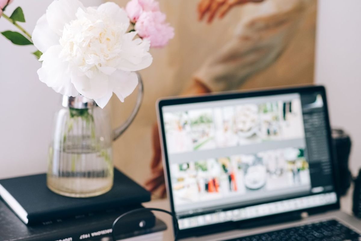 Laptop displaying a photo gallery beside a vase of flowers