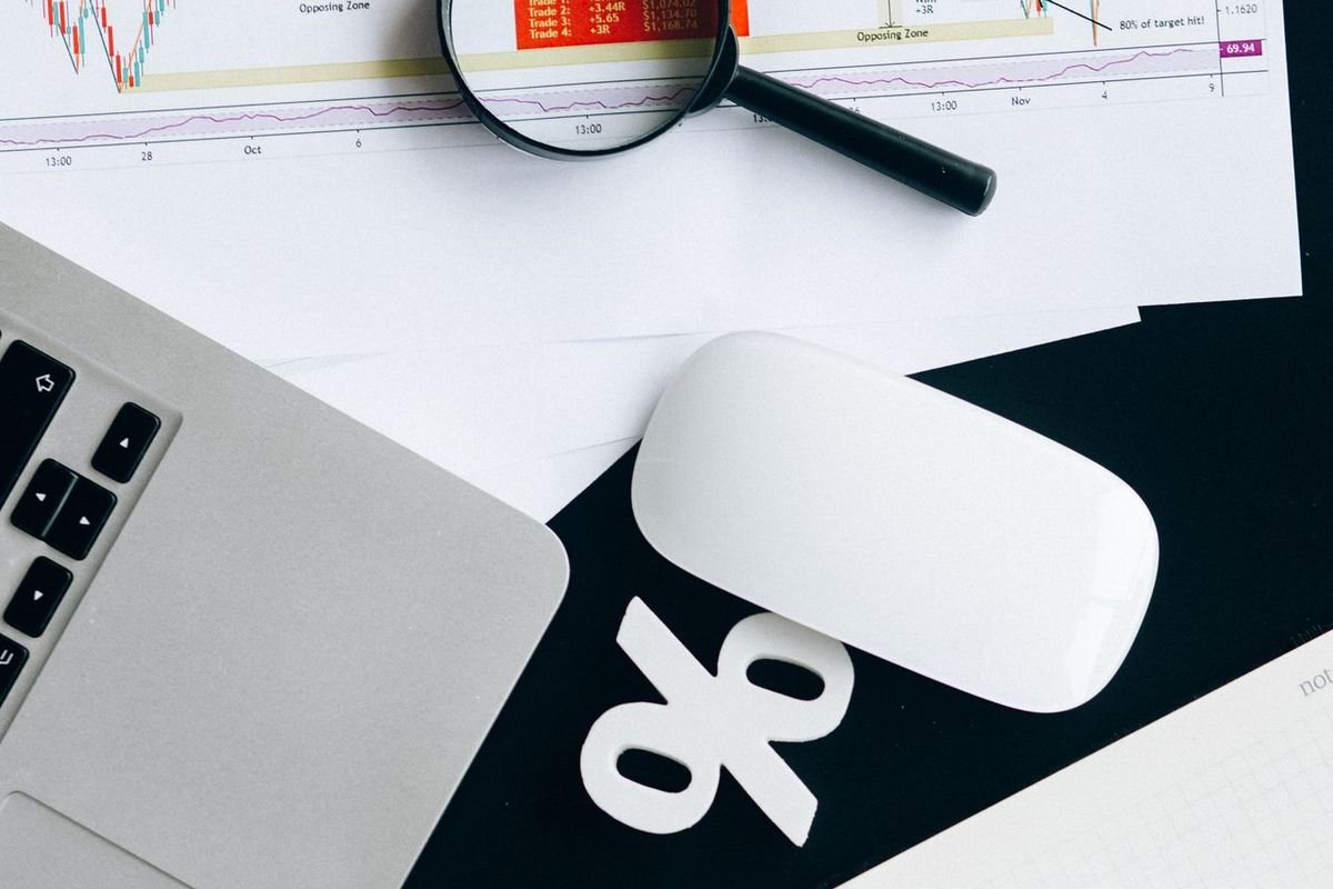 Laptop, mouse and a magnifying glass over printed charts on a desk