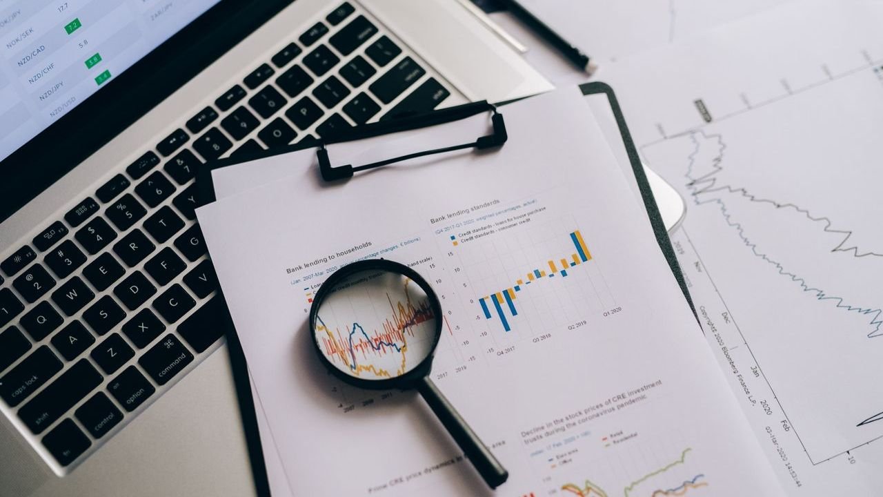 Magnifying glass over a clipboard of charts beside an open laptop