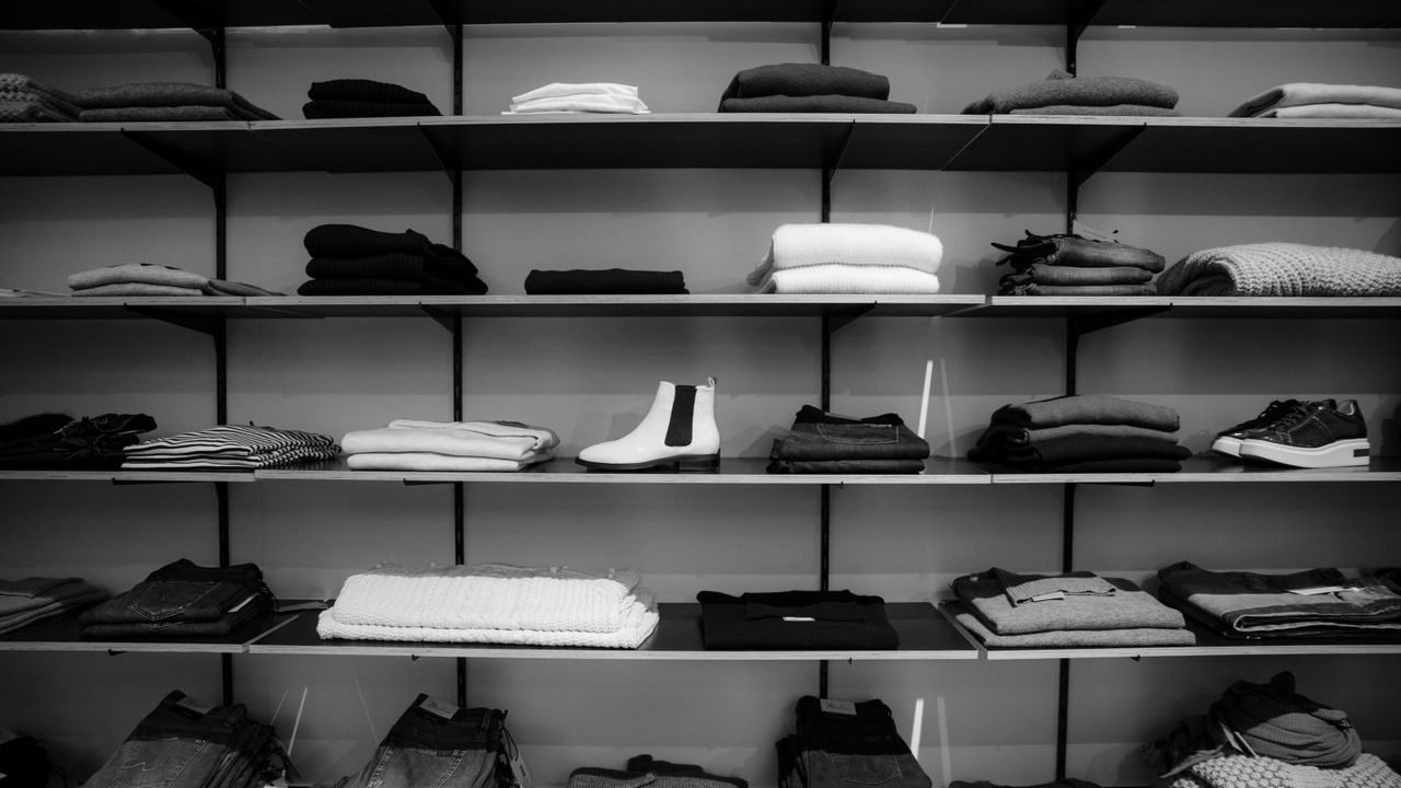 Black and white photo of folded clothes and shoes on store shelves