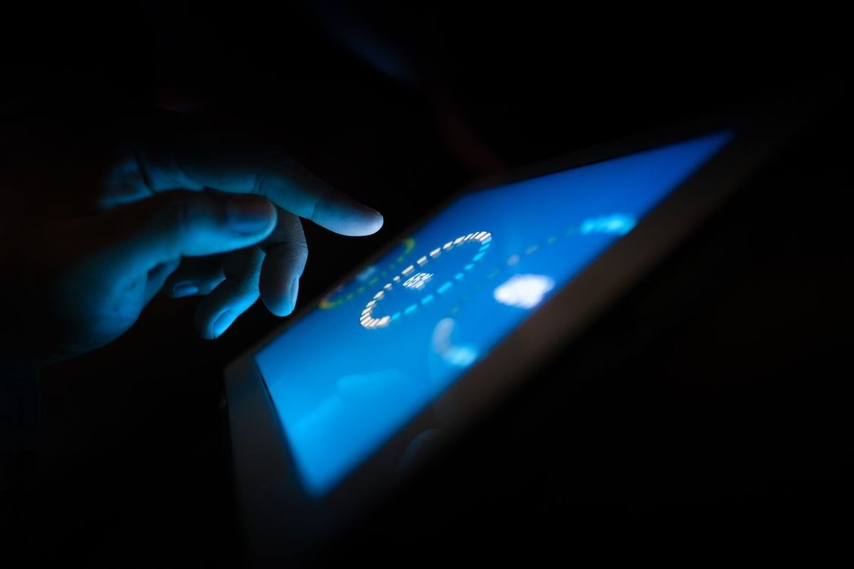 Person touching a glowing tablet screen in the dark