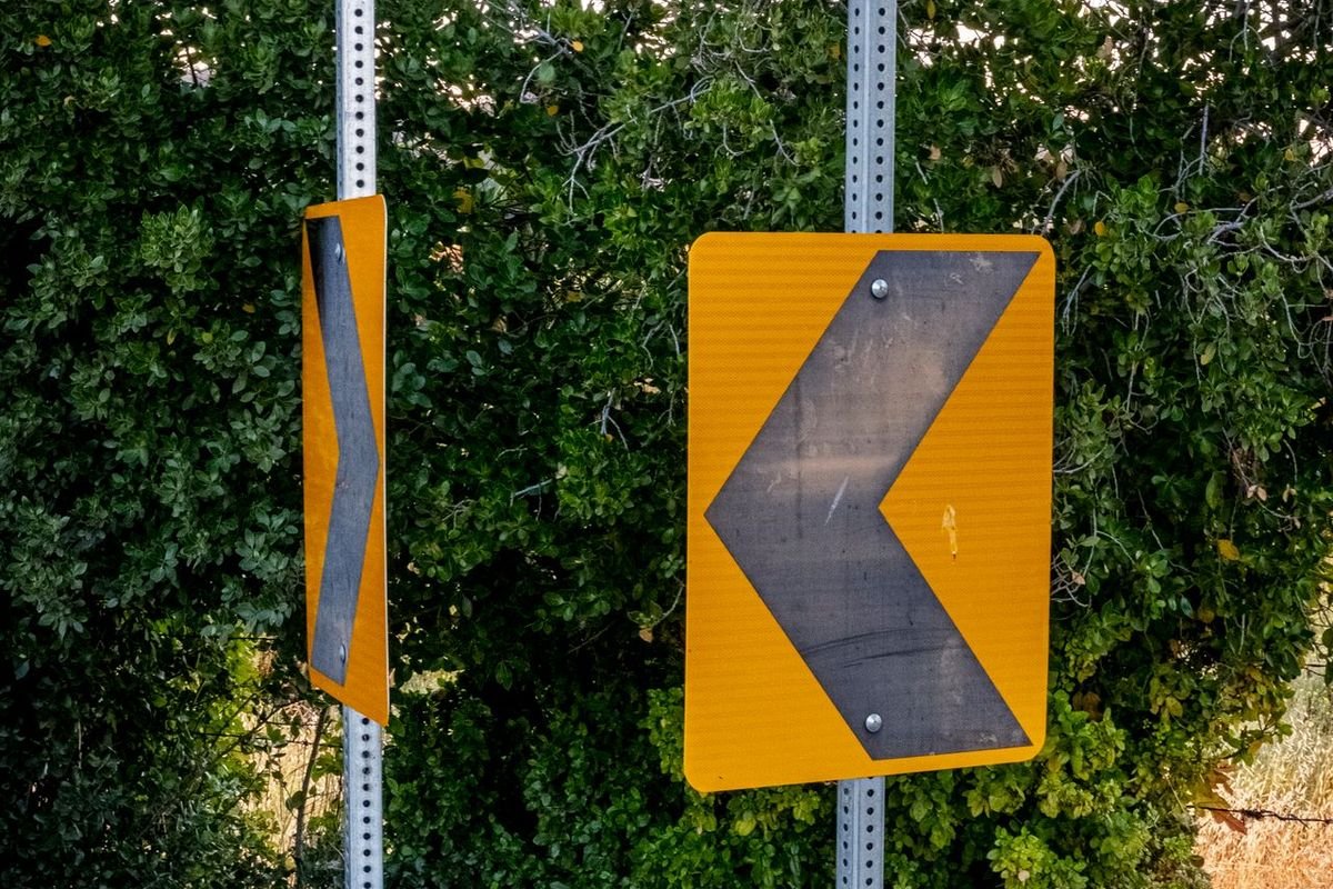 Yellow chevron road signs pointing left among green foliage