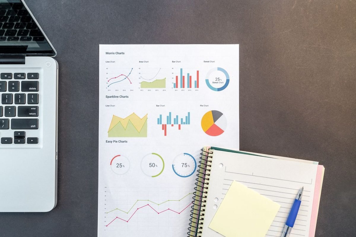 Printed charts and a notebook beside a laptop on a desk