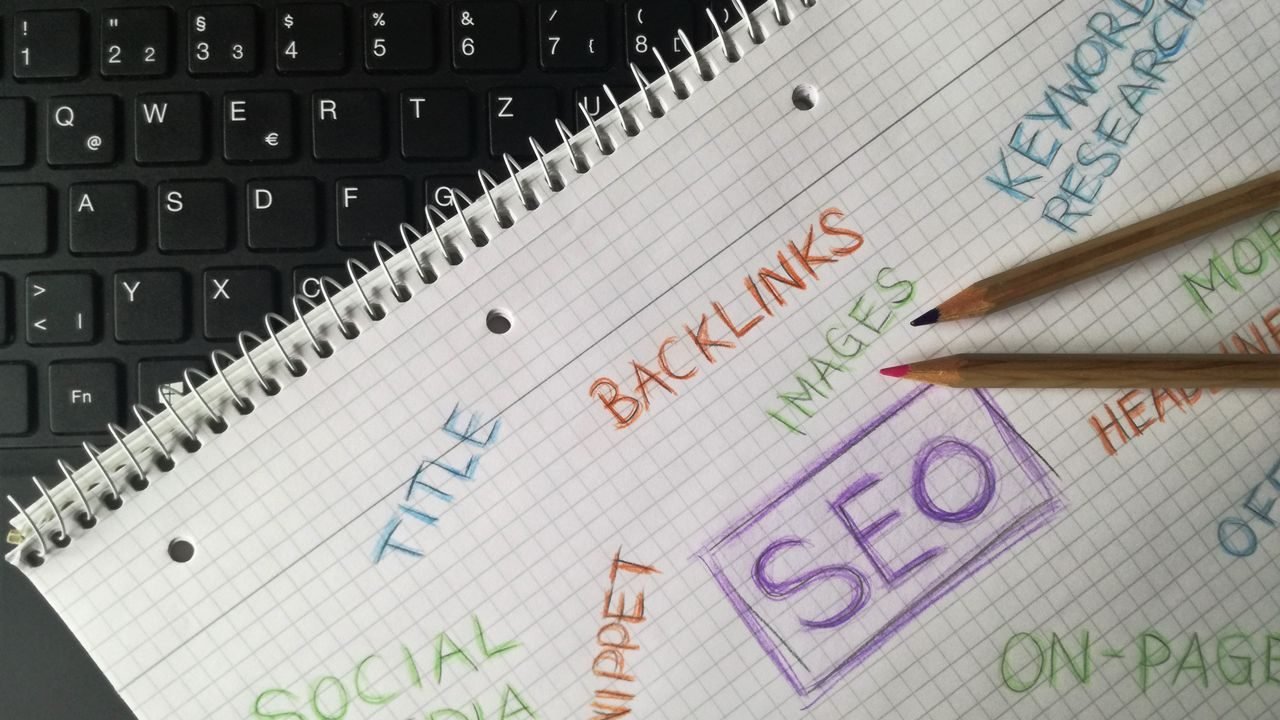 Notebook on a keyboard with handwritten SEO terms such as keyword research, backlinks and on-page