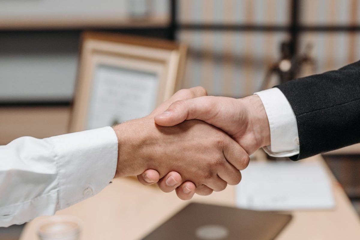 Two people shaking hands across a desk in an office