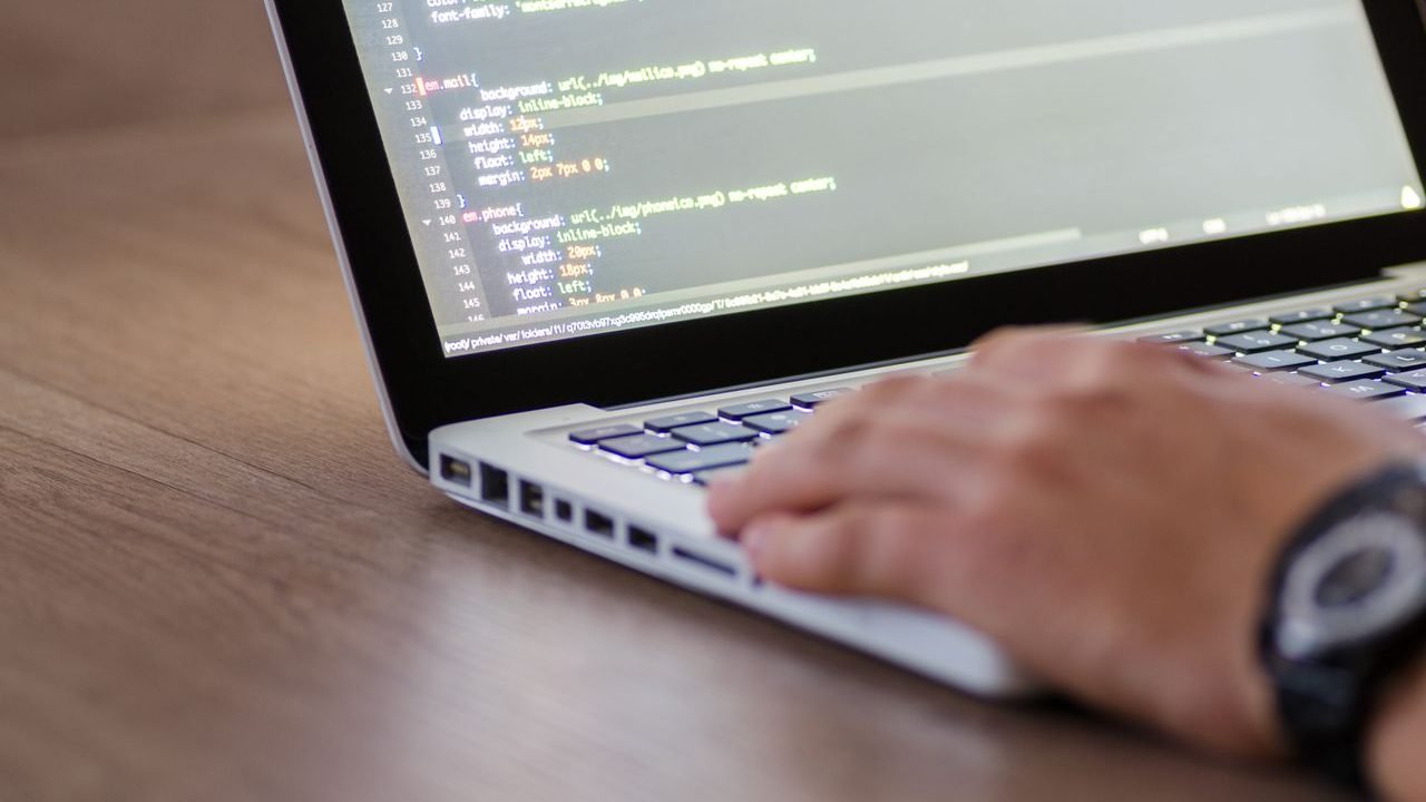 Hands typing on a laptop with source code open on the screen