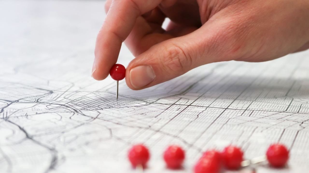 Hand placing a red pin on a street map