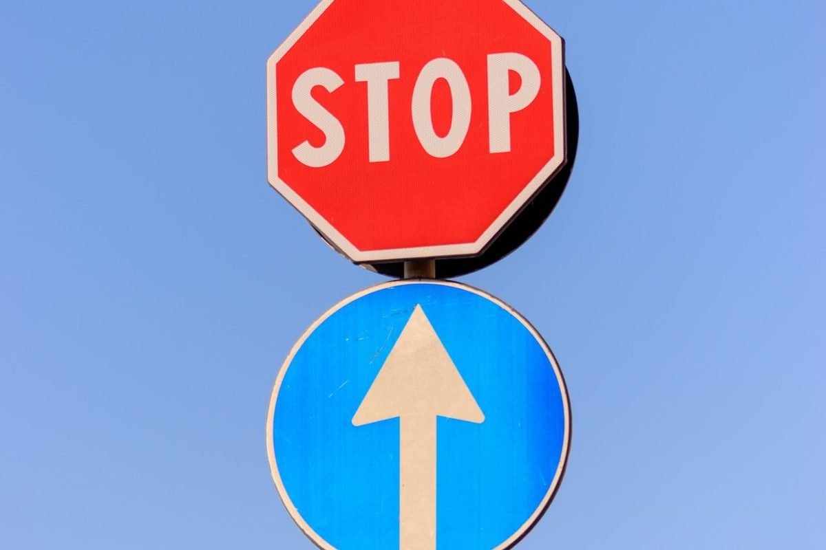Red stop sign above a blue arrow sign against a clear sky