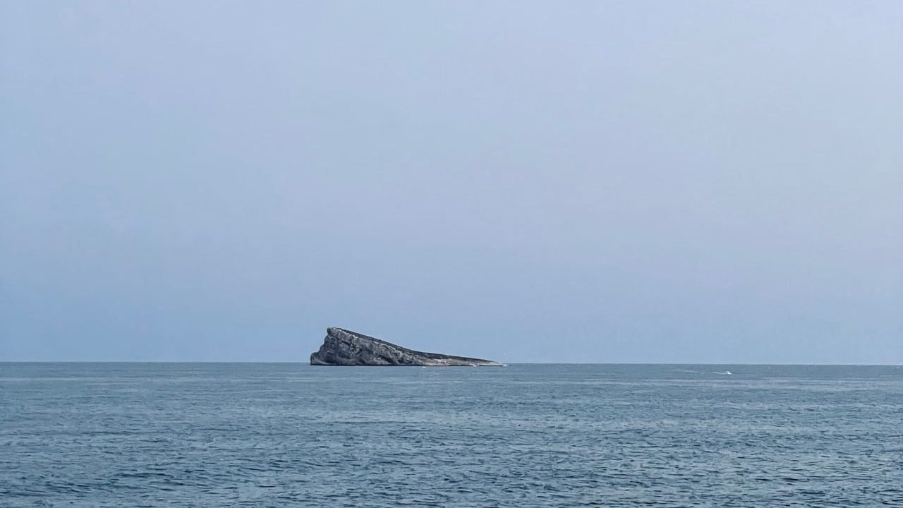 Distant island rising from a calm sea under a pale sky