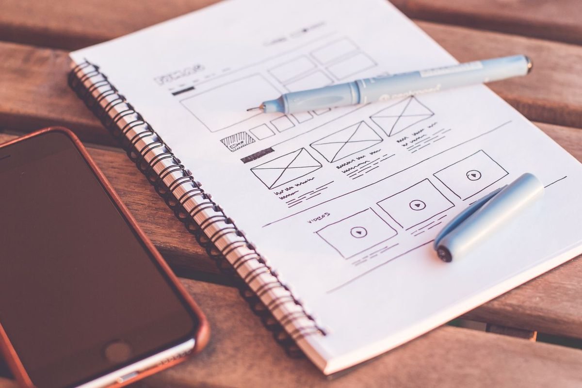 Notebook with wireframe sketches beside a smartphone on a wooden desk