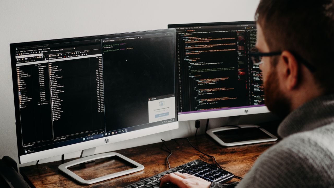 Developer typing at a desk with two monitors showing code