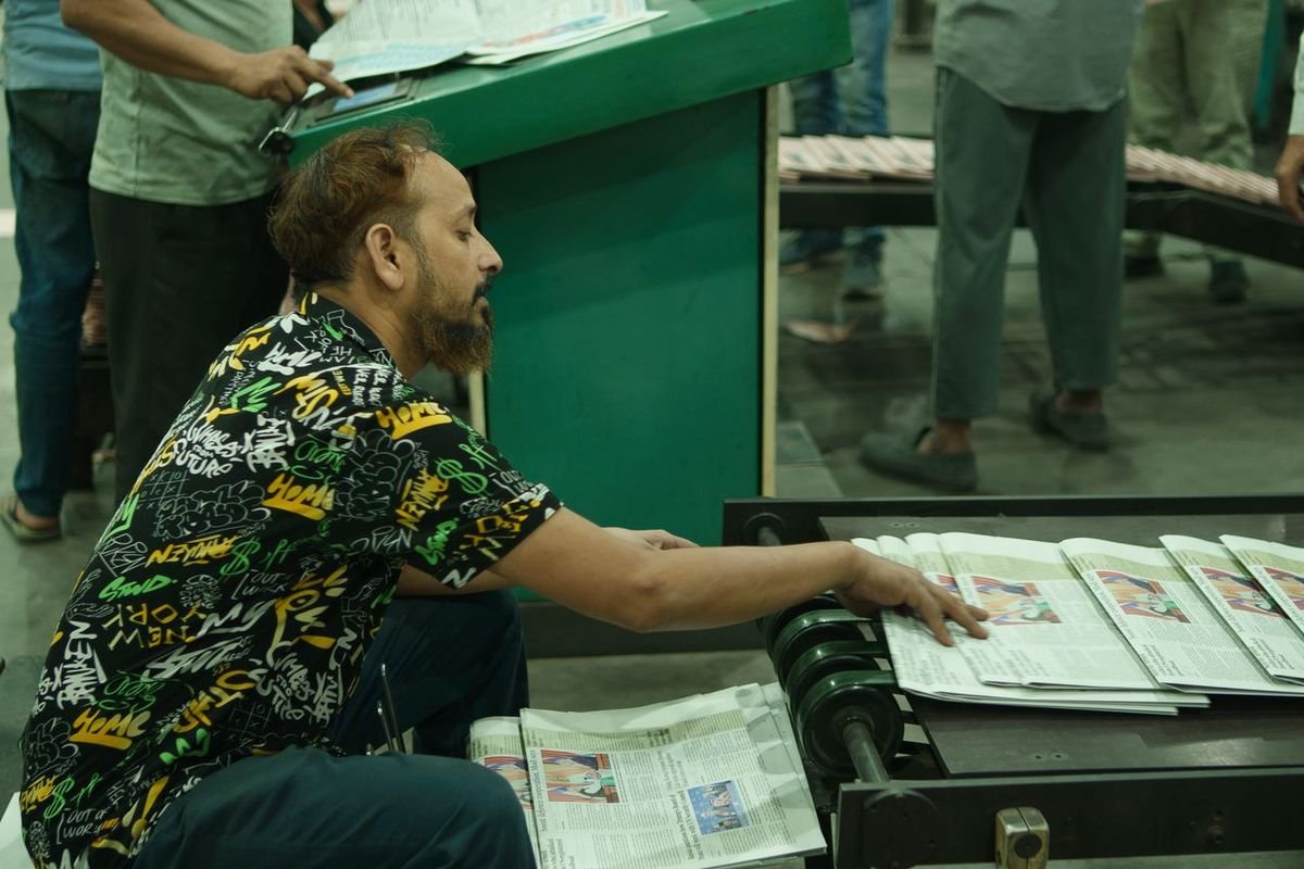Man handling printed newspapers at a press machine