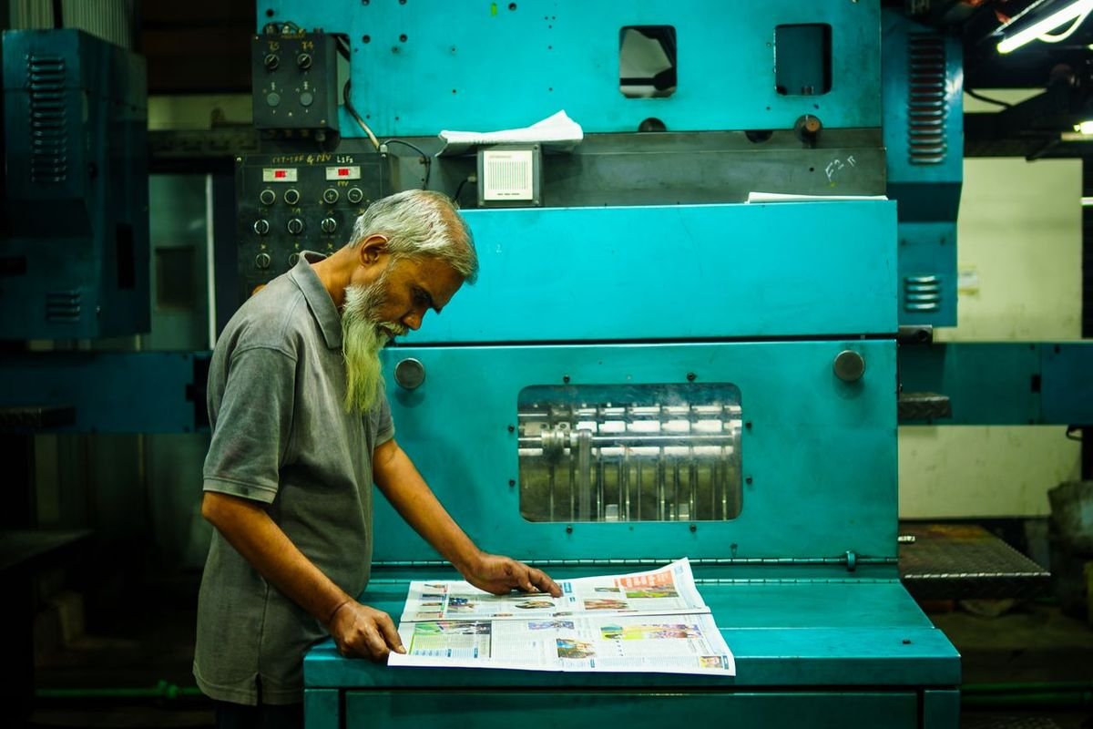 Worker checking freshly printed pages at a teal printing press