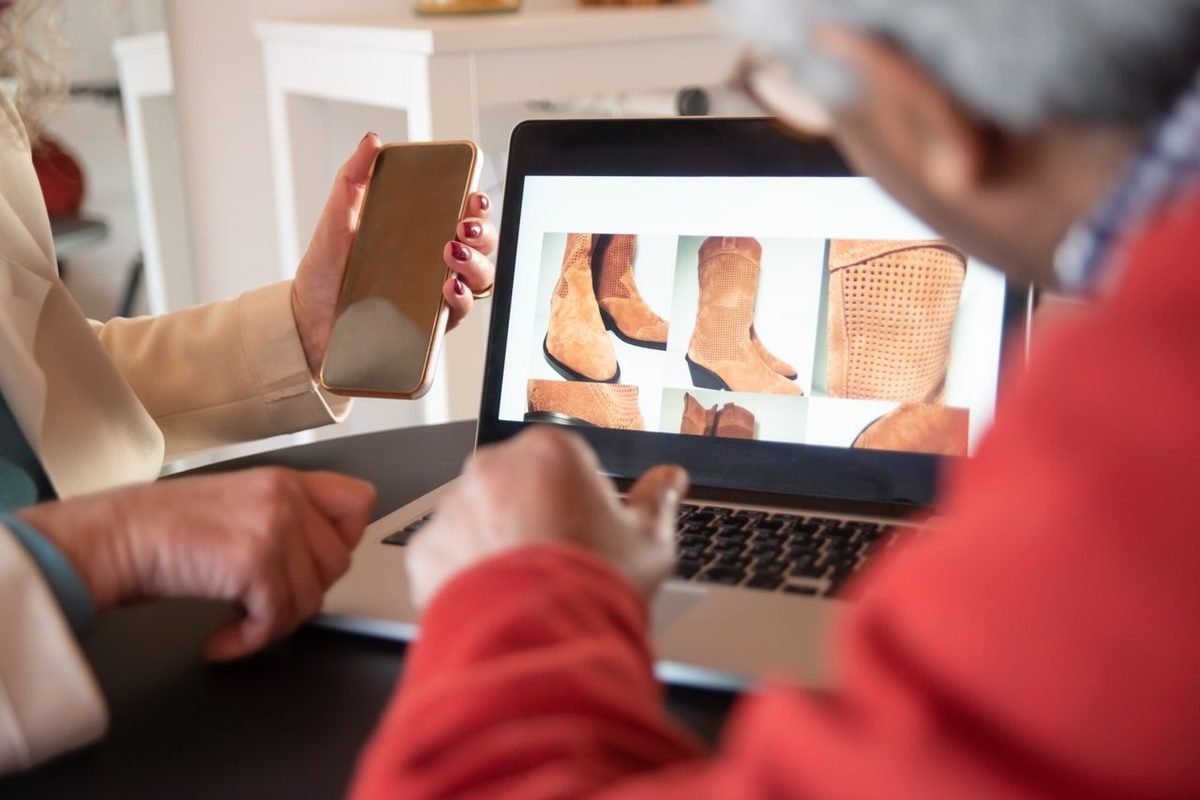 Two people comparing shoes on a laptop and smartphone