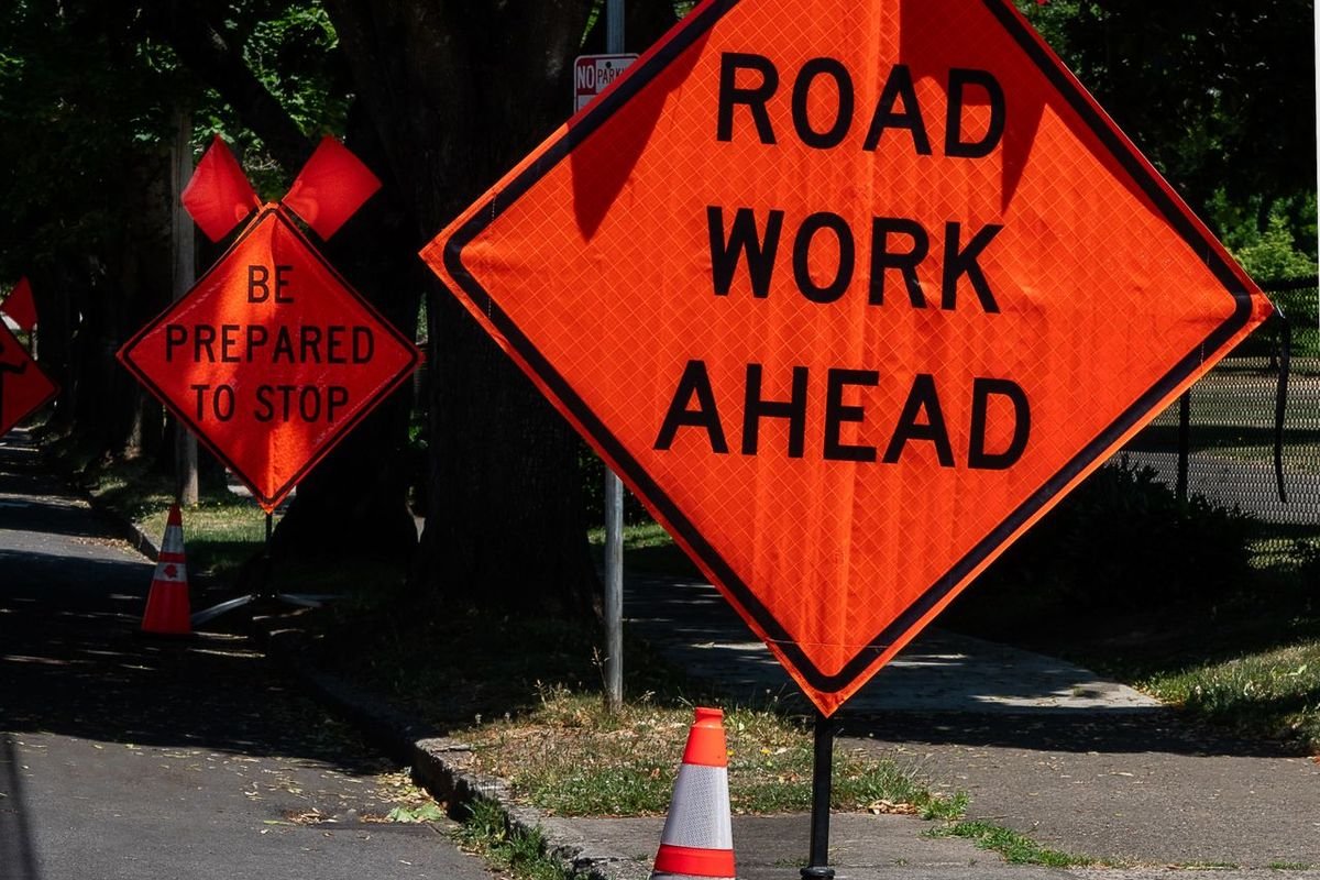 Orange road work ahead sign beside traffic cones