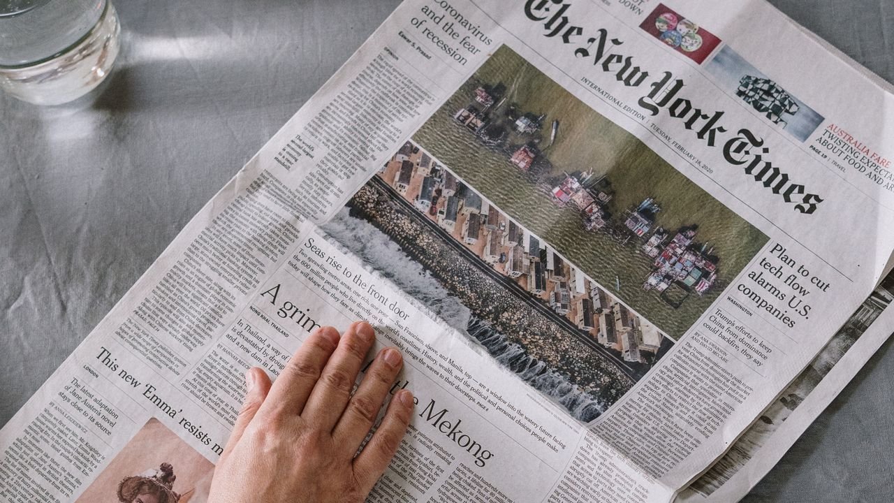 Hand resting on a newspaper page with a headline and photograph