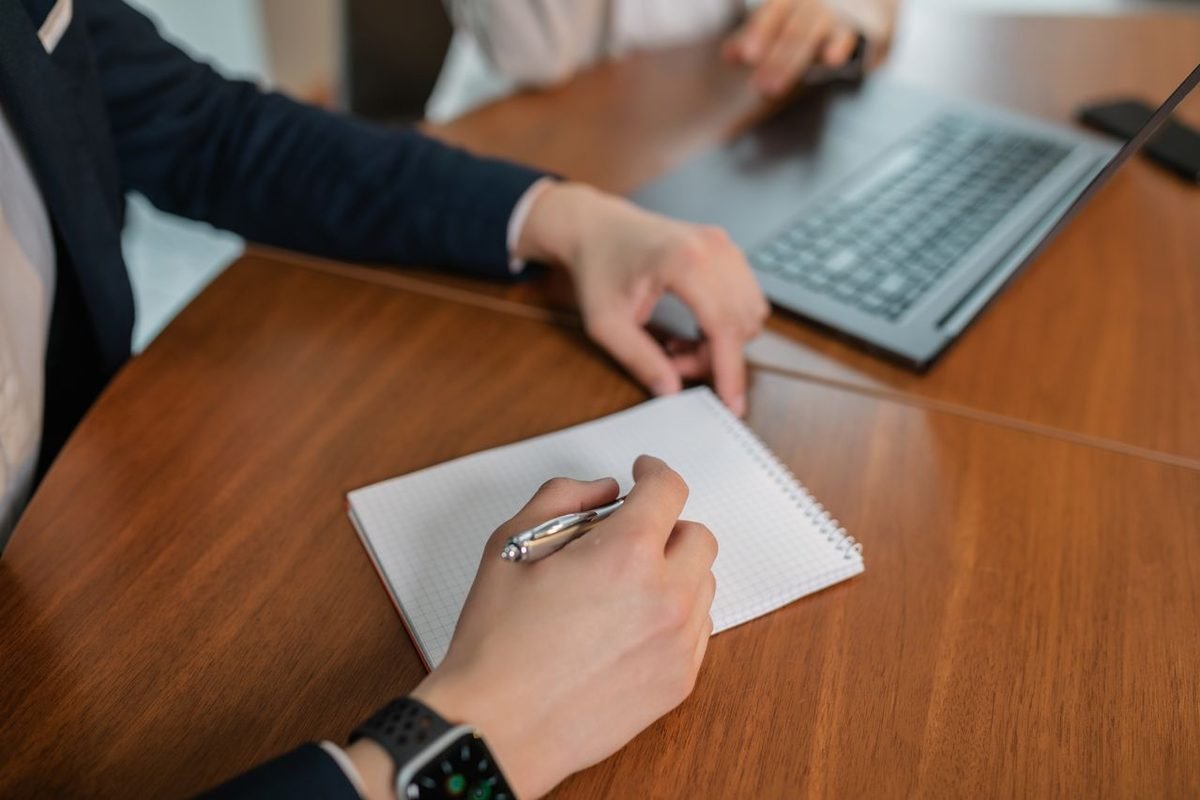Hand writing notes on paper beside a laptop