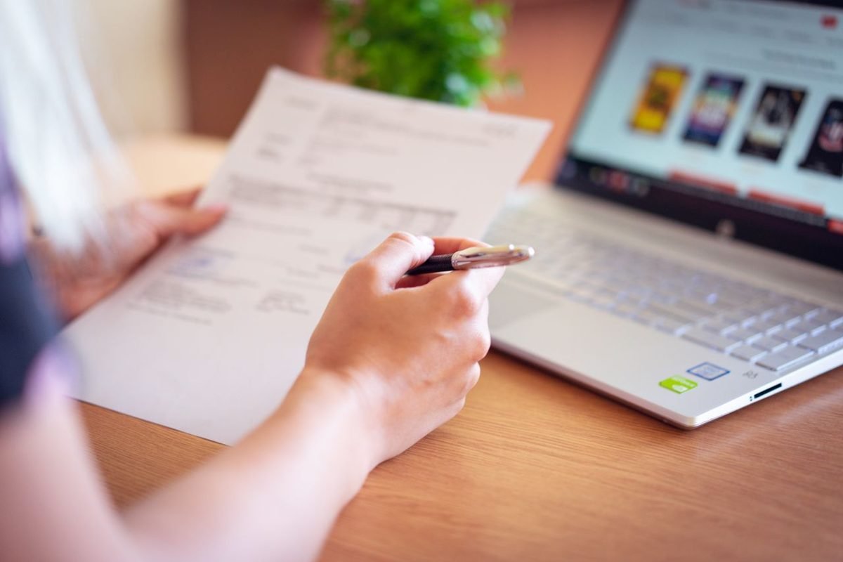 Person filling in a form with a pen beside a laptop